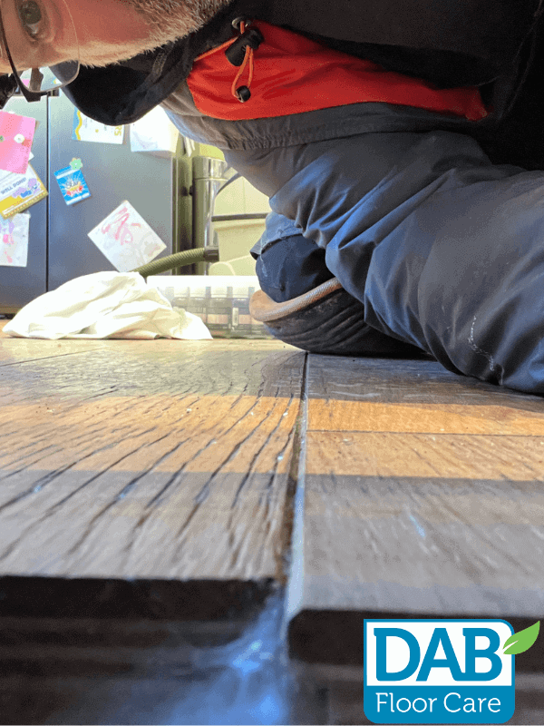 Person inspecting wooden floor closely.